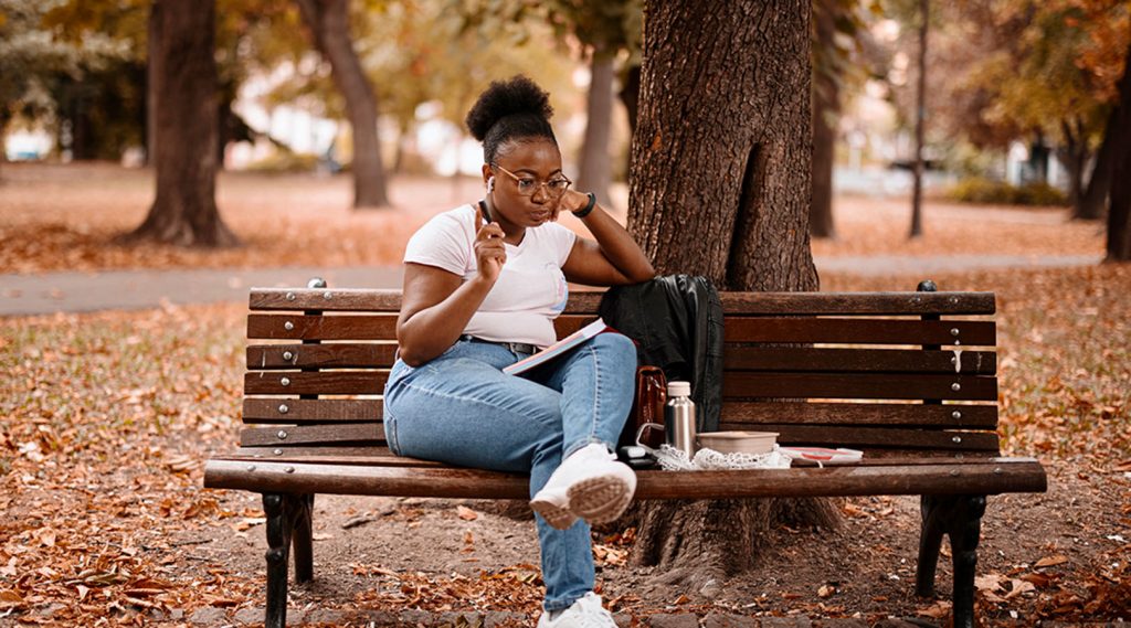 Young adult sitting outside on a bench with a notebook