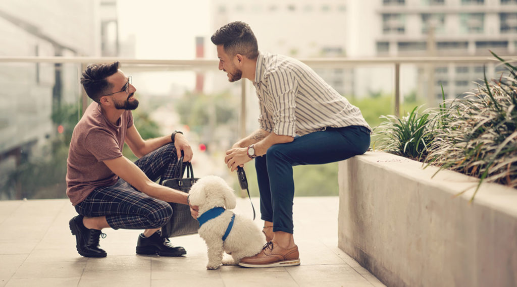 Two young adults sitting down outside and petting a dog