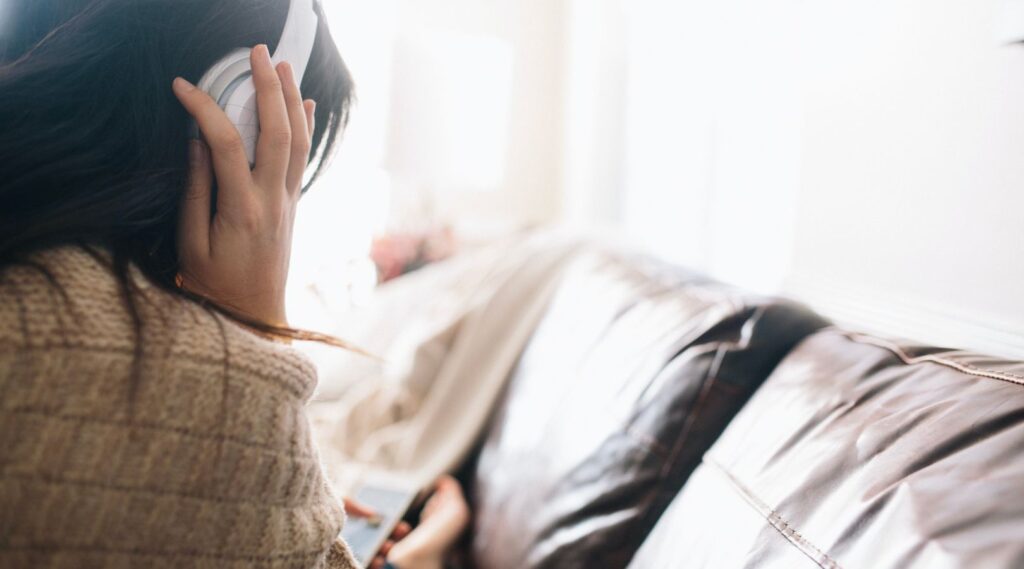 A post-secondary student with headphones on a couch reflecting on information about self-harm